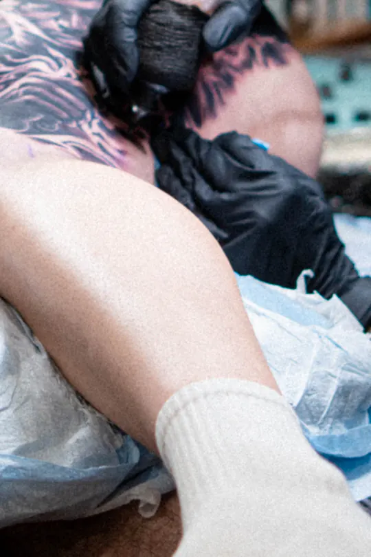 Gros plan des mains gantées d’un artiste en train de tatouer.