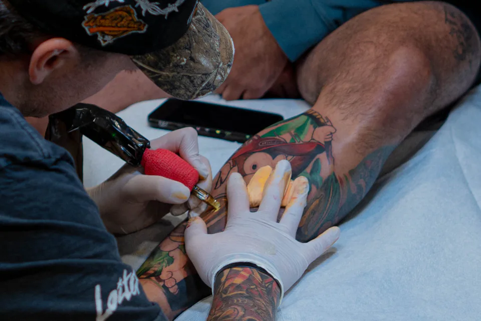 Artista del tatuaje añadiendo color a un tatuaje grande en la pierna.